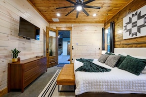 A wooden interior with a bed, a dresser, a television, and a ceiling fan. - The Gather House | Private Pool • Sauna • Game Room • UTV Trail Access • Sleeps 26 (Broken Bow)