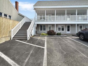 Ein zweigeschossiges Gebäude mit überdachter Veranda, Treppe und Parkplatz.