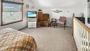 Quarto com cama, televisão, cadeira, escrivaninha, janela com vista e ventilador de teto.