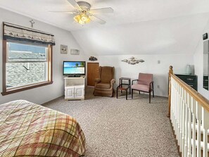 Ein Schlafzimmer mit einem Bett, einem Fernseher, einem Sessel, einem Schreibtisch, einem Fenster mit Aussicht und einem Deckenventilator.