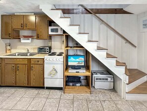 A compact kitchen with wooden cabinets, a microwave, a stove, and a television on a shelf. - Walk to Wells Beach | Cozy 1BR w/ Loft Condo (Wells)