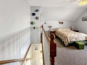 A bedroom with a bed, a nightstand, a lamp, a staircase, and wall decorations. - Walk to Wells Beach | Cozy 1BR w/ Loft Condo (Wells)