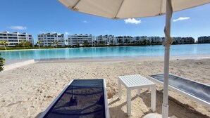 A beach with a pool, white lounge chairs, and a clear blue sky. - Beach Boho Retreat 2BR Private Jacuzzi Downtown Punta Cana City Place (Punta Cana)