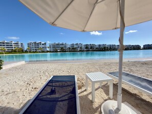 Ein Strand mit Schwimmbad, weißen Liegestühlen und wolkenlosem, blauem Himmel.