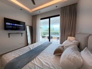 Ein Hotelzimmer mit Bett, Wandfernseher, Balkon mit Tisch und Stühlen und Blick ins Freie.