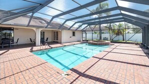 Ein überdachter Pool mit Glasdach, Backsteinböden und einer Terrassenfläche mit Sitzgelegenheiten.