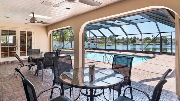 Eine Außenpatio mit Pool, der durch Glas geschützt ist, Essbereich mit Tischen und Stühlen sowie Deckenventilatoren.