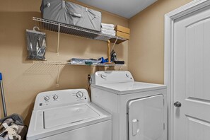 A laundry area with a washing machine, dryer, and shelves above holding folded clothes and a bag. - Bearfoot Beech - Game table, fire pit, private hot tub! (Banner Elk)