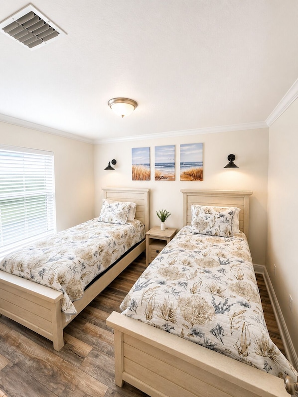 A bedroom with two beds, a ceiling vent, wall-mounted lamps, and a window with blinds.