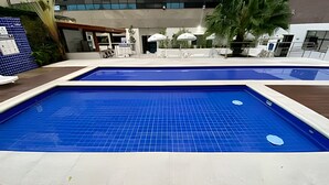 Ein Schwimmbecken mit gefliestem Sonnendeck und einer überdachten Sitzgruppe mit Sonnenschirmen.