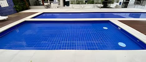 A swimming pool with a tiled deck and a covered seating area with umbrellas.