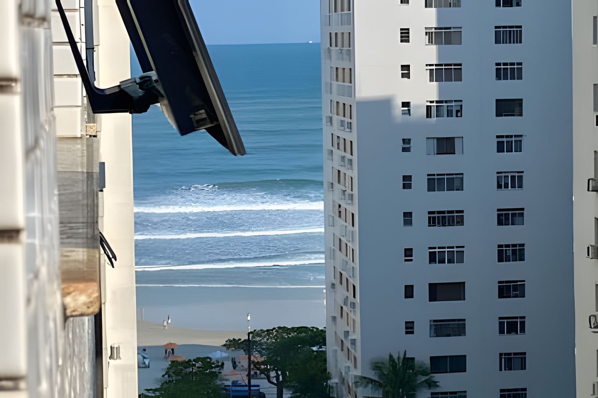 A high-rise building with multiple windows and balconies overlooking a beach with waves.