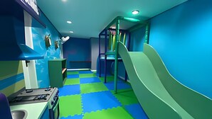 Un área de juegos infantiles con un tobogán, paredes coloridas y suelo a cuadros.