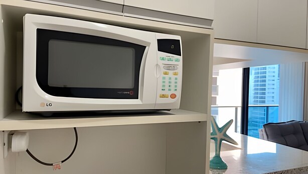 Un microondas en un estante en una cocina con un adorno de estrella de mar y vistas a edificios.