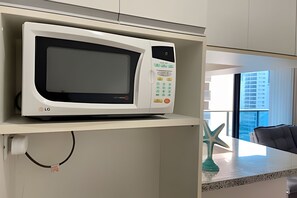Un forno a microonde su uno scaffale in una zona cucina, con una decorazione a stella marina e vista sugli edifici esterni.