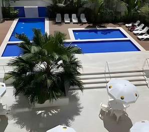 A pool area with two rectangular pools, lounge chairs, and a palm tree. - SHB Joia de Pitangueiras lazer completo (Guarujá)