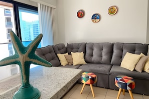 A modern living room with a grey sectional sofa, a starfish decoration, and colorful stools. - SHB Joia de Pitangueiras lazer completo (Guarujá)