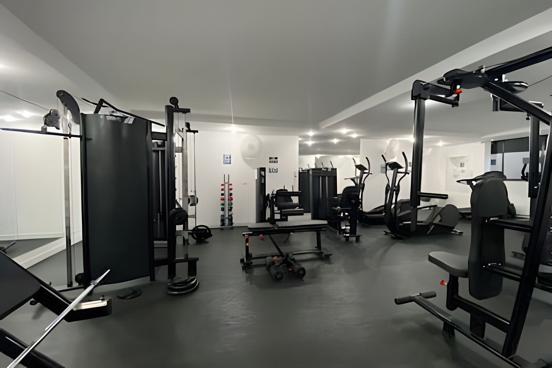 Ein Fitnessstudio mit verschiedenen Trainingsgeräten, darunter ein Squat-Rack, eine Hantelbank und Laufbänder.