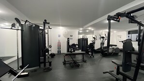 Ein Fitnessstudio mit verschiedenen Trainingsgeräten, darunter ein Squat-Rack, eine Hantelbank und Laufbänder.