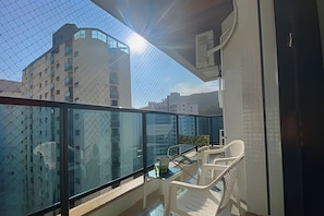 A balcony with a glass railing, a table, and white chairs. - SHB Joia de Pitangueiras lazer completo (Guarujá)