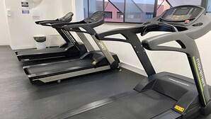 Tres cintas de correr en un gimnasio de diseño moderno, con un amplio ventanal y un interior limpio y minimalista.