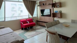 Een moderne woonkamer met een flatscreen televisie, rode stoelen, een eettafel en een balkon met uitzicht.