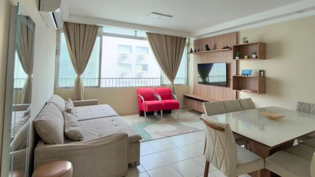 Een moderne woonkamer met een bank, rode stoelen, een eettafel en een tv die aan de muur is bevestigd.