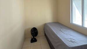 Een kleine kamer met een enkel bed, een ventilator en een raam.