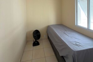 A small, single-bed room with a fan and a window. - Fully Furnished Apartment in the Heart of Pitangueiras, Spacious Apartment in Guarujá (Guarujá)