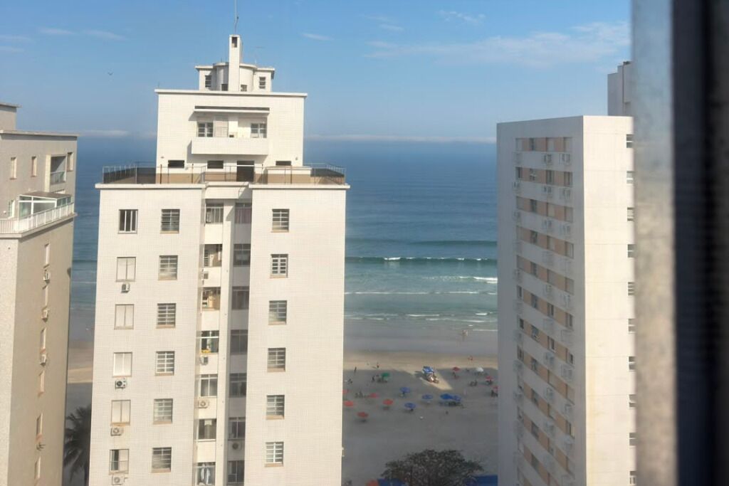 A high-rise building with multiple floors, a balcony on the top floor, and a view of the beach with umbrellas.