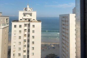 Ein Hochhaus mit mehreren Stockwerken, einem Balkon im obersten Geschoss und Blick auf den Strand mit Sonnenschirmen.