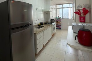 A modern kitchen with a stainless steel refrigerator, a sink, and a red kettle on the counter. - Fully Furnished Apartment in the Heart of Pitangueiras, Spacious Apartment in Guarujá (Guarujá)