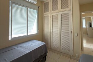 Ein Schlafzimmer mit einem Bett, einem Fenster mit Jalousien und einer Reihe von Schrankflügeln.