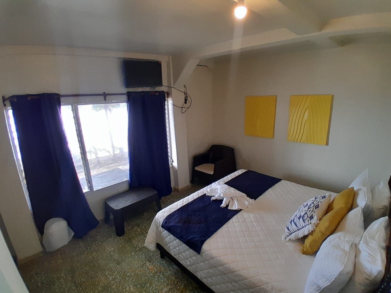 Un dormitorio con cama, una banca, una silla y una ventana con cortinas.