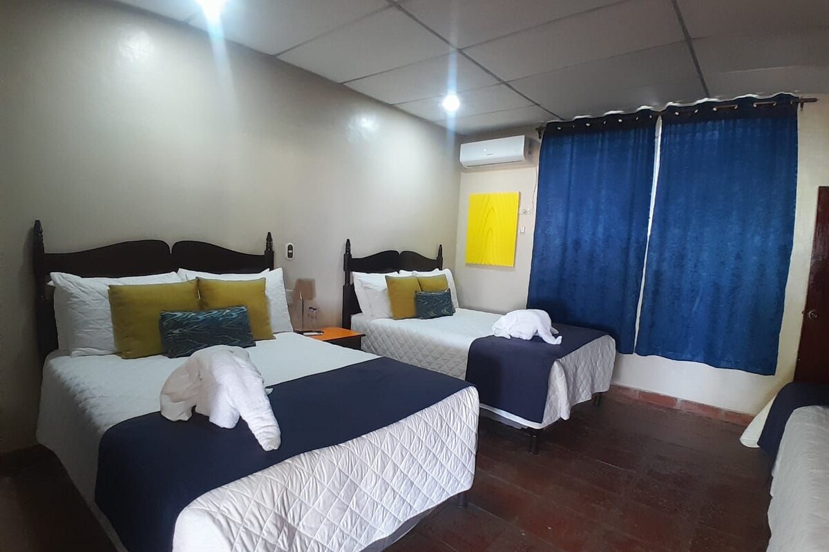 A hotel room with two beds, a small table, and an air conditioning unit.