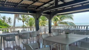 An outdoor covered patio with white tables and chairs, a view of the ocean, and palm trees.