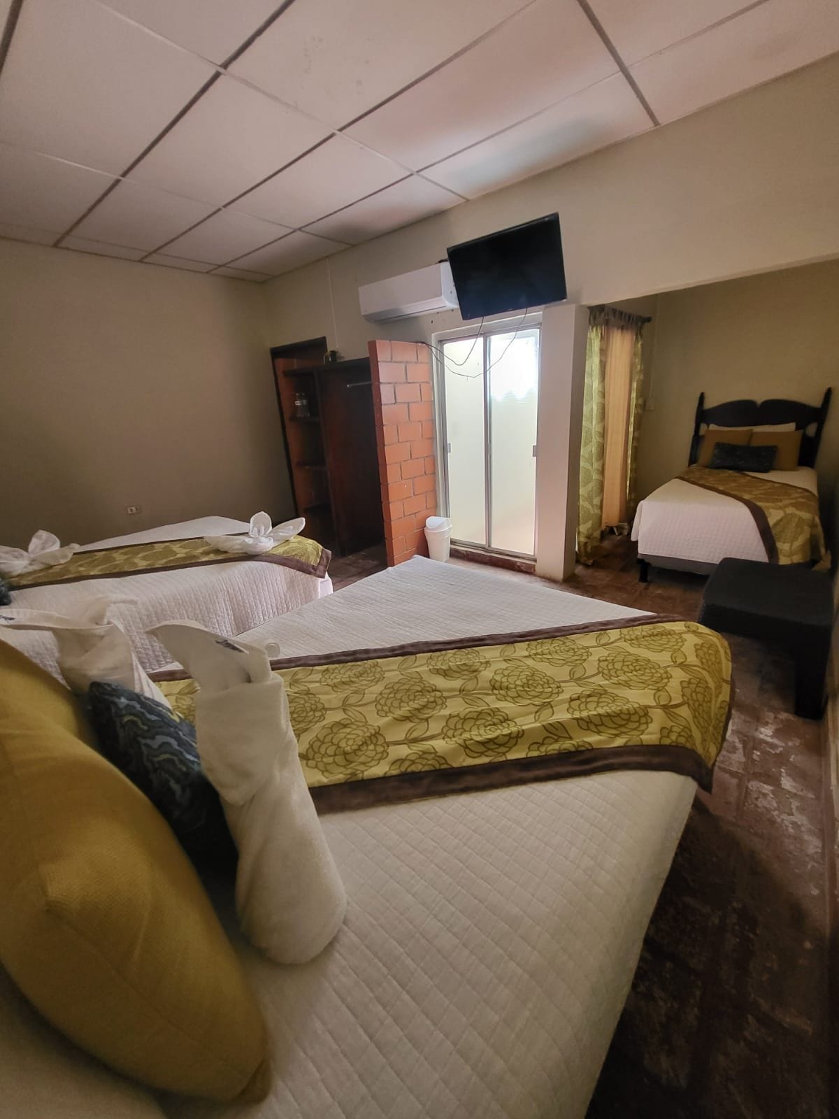 Habitación de hotel con dos camas, un pequeño rincón de descanso, un ventanal corredero y un televisor.
