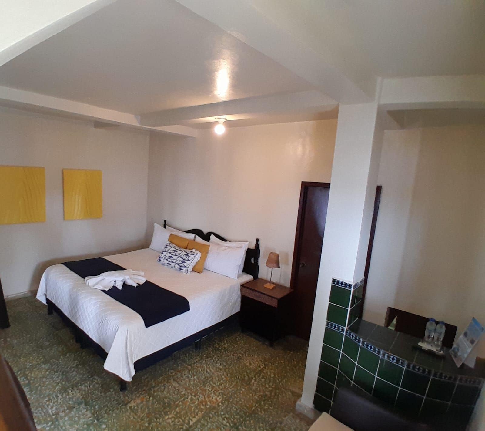 Une chambre d’hôtel avec un lit, une table de chevet, une lampe et un mur recouvert de carreaux.