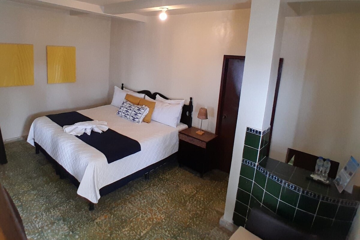 A hotel room with a bed, bedside table, lamp, and a tiled wall.