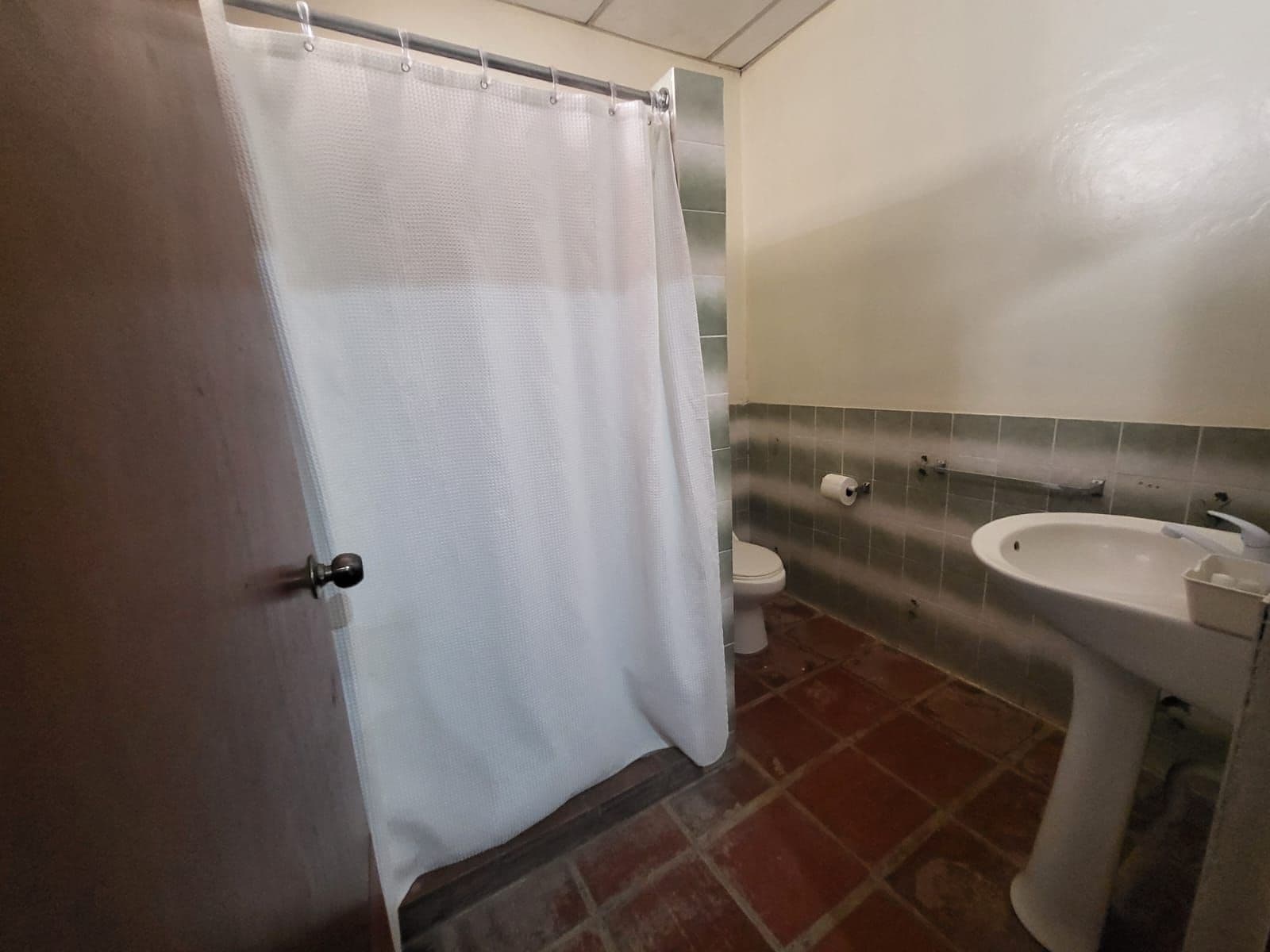 Een badkamer met douchegordijn, toilet, wastafel en betegelde wanden.