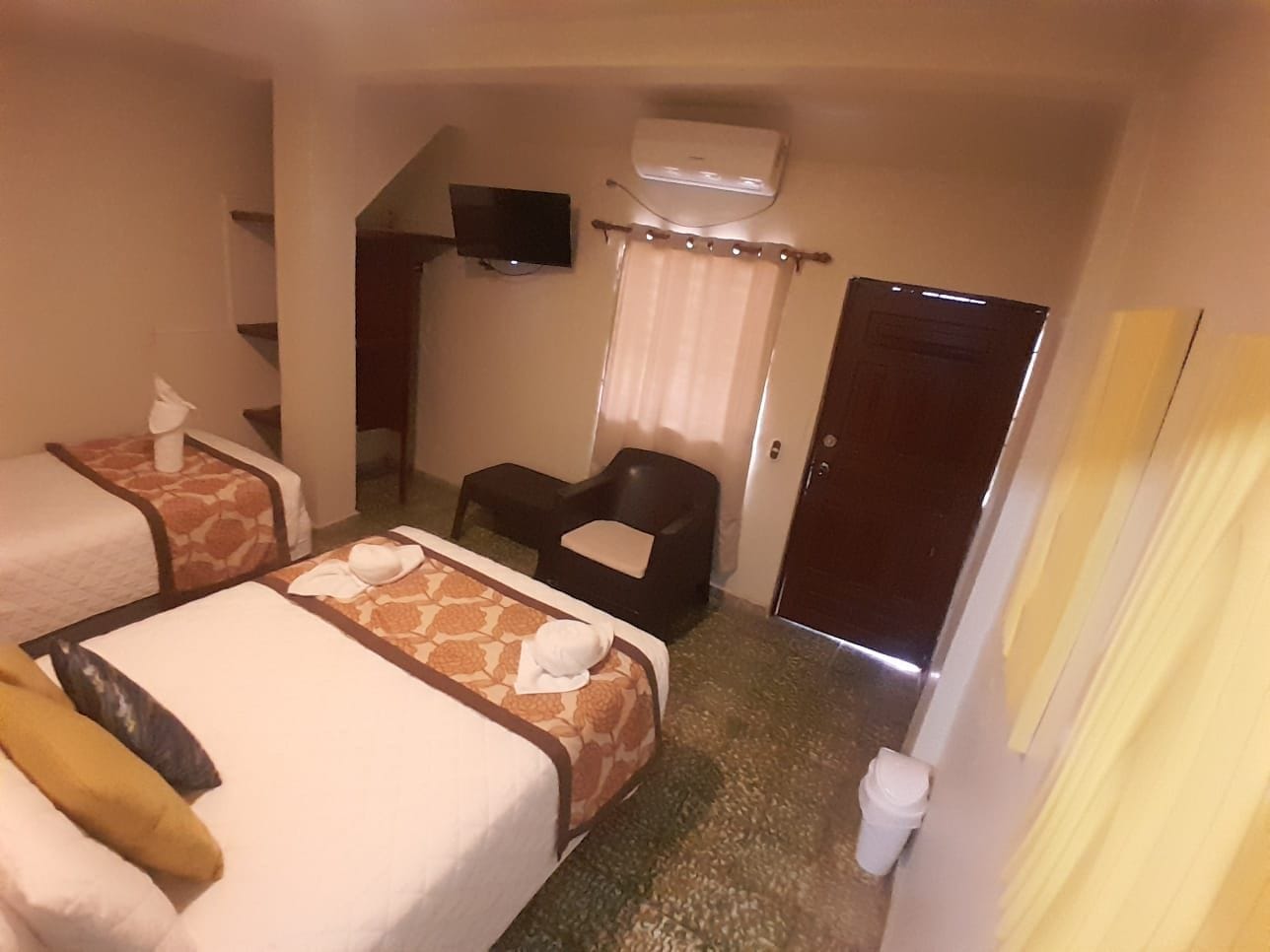 Habitación de hotel con dos camas, televisión, aire acondicionado, una silla y una puerta.