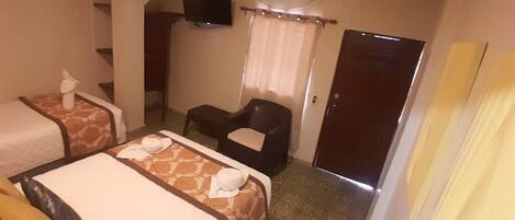 Habitación de hotel con dos camas, televisión, aire acondicionado, una silla y una puerta.