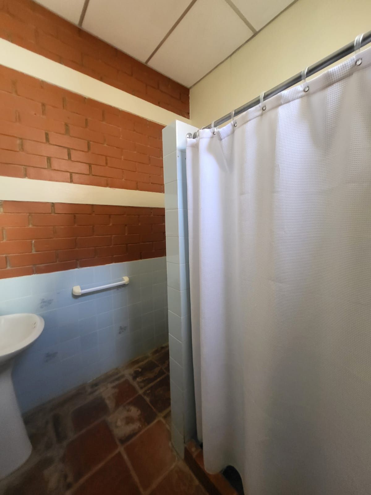 A bathroom with a white sink, a towel rack, a shower curtain, and a tiled floor.