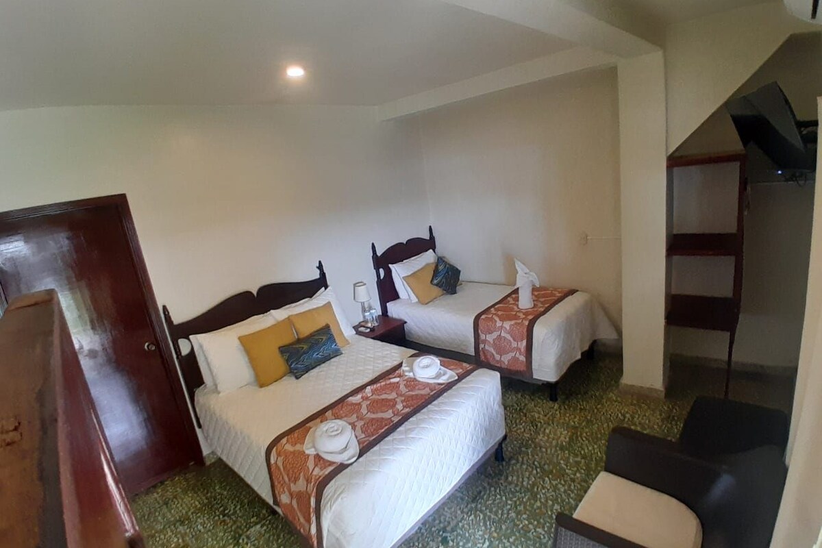 A hotel room with two beds, a wooden door, a small table, a chair, and a staircase.
