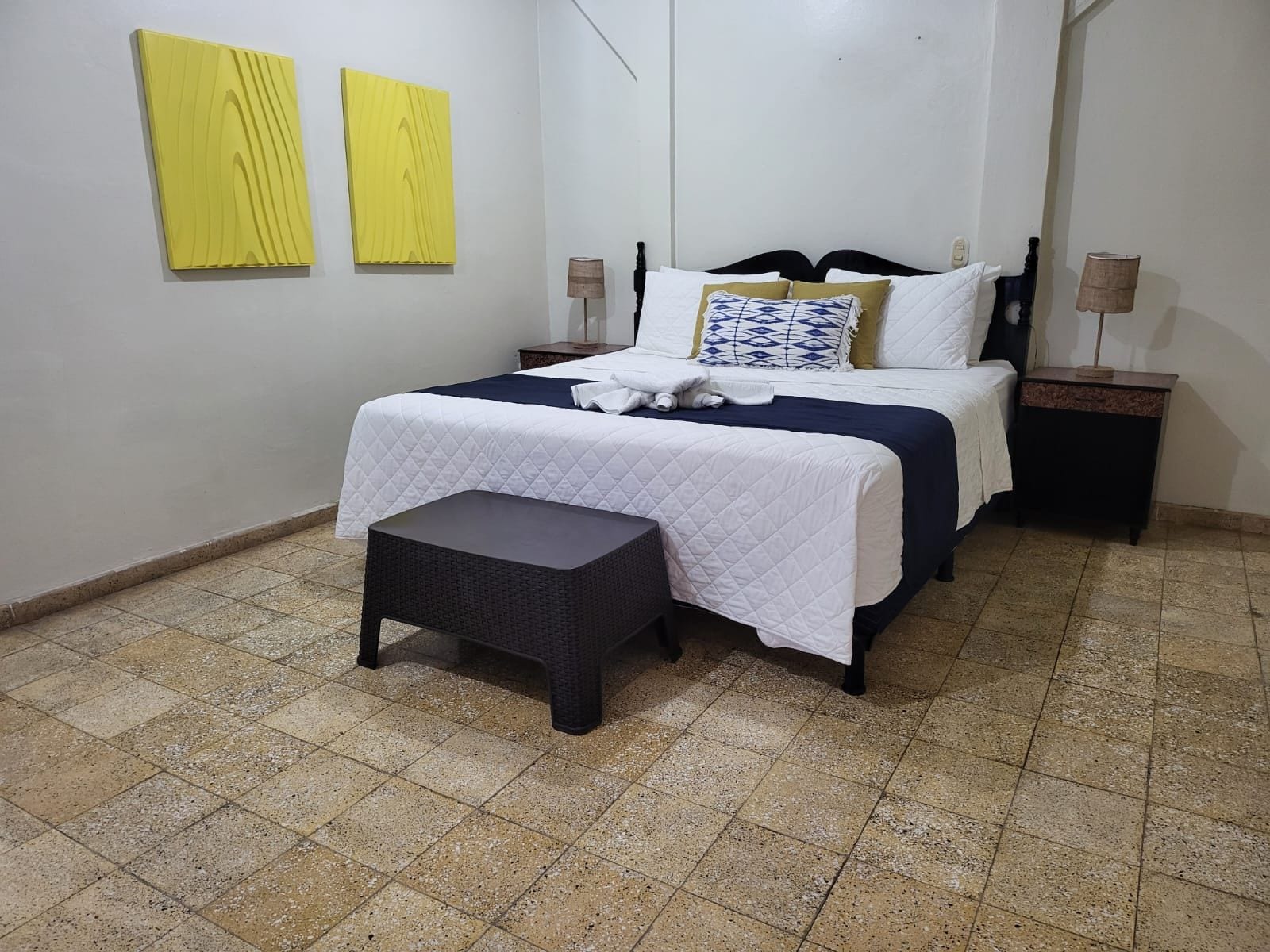 A hotel room with a bed, bedside tables, a bench, and two wall-mounted lamps.