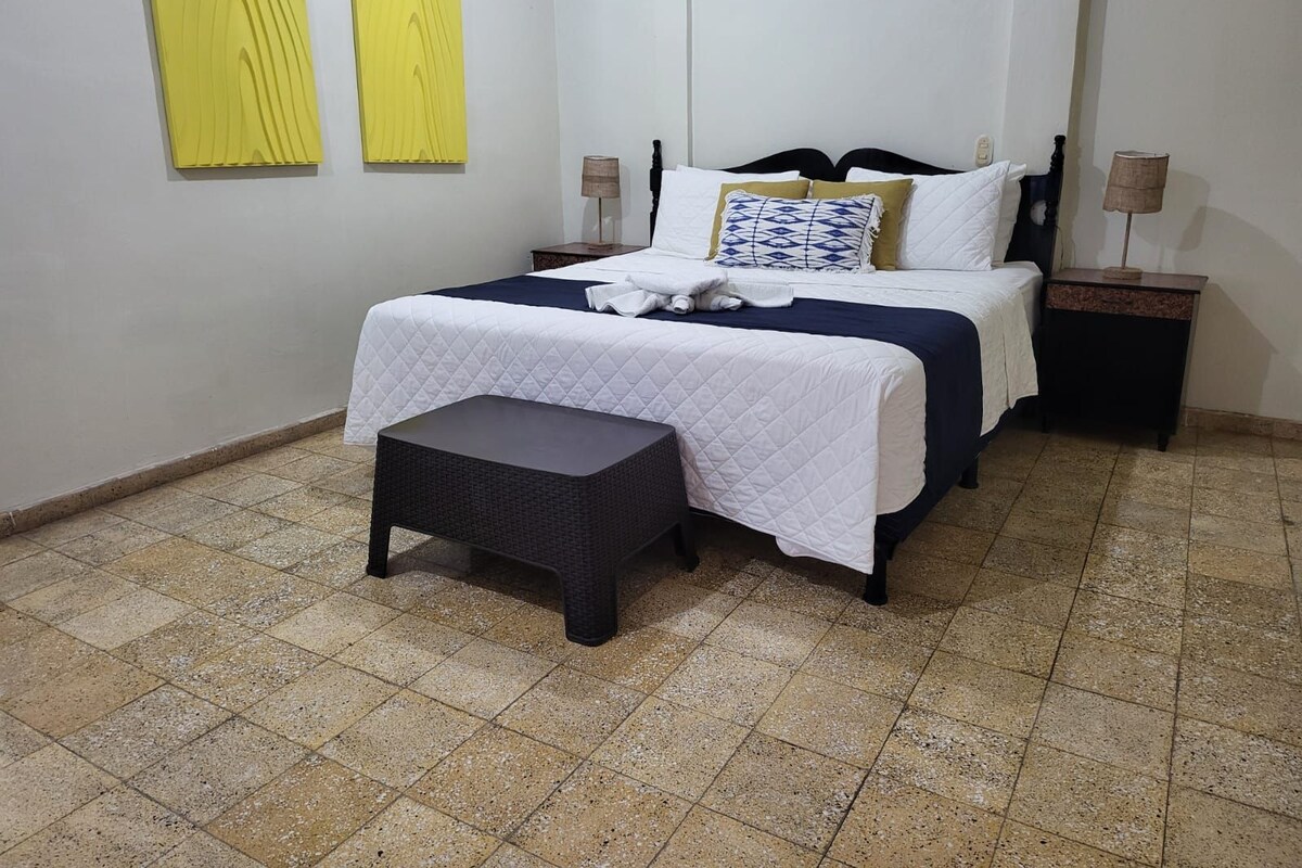 A hotel room with a bed, bedside tables, a bench, and two wall-mounted lamps.