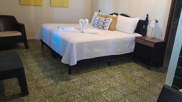 A hotel room with a bed, two chairs, a nightstand, and a wall with two yellow artworks.