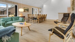 Un amplio salón con un sofá verde, una mesa de comedor de madera y un sillón de cuero negro.