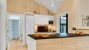 Una cocina moderna con paneles de madera, encimera negra, microondas empotrado y refrigerador.
