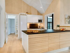 Eine moderne Küche mit Holzvertäfelung, einer schwarzen Arbeitsplatte, einer eingebauten Mikrowelle und einem Kühlschrank.